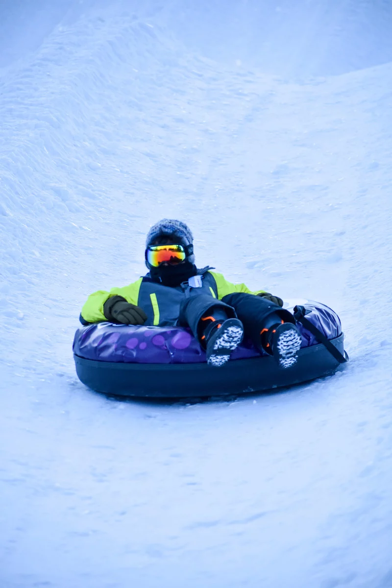 Young snow tube rider in googles & snowsuit sliding down the hill at Bousquet Mountain