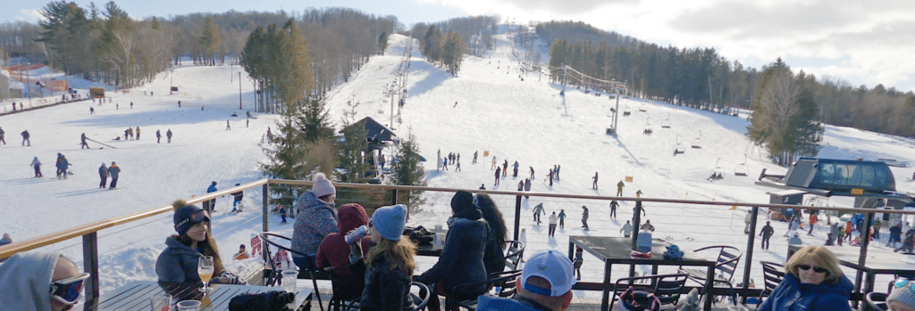 Skiers hanging out on deck of Bousquet Mountain lodge, looking at the slopes