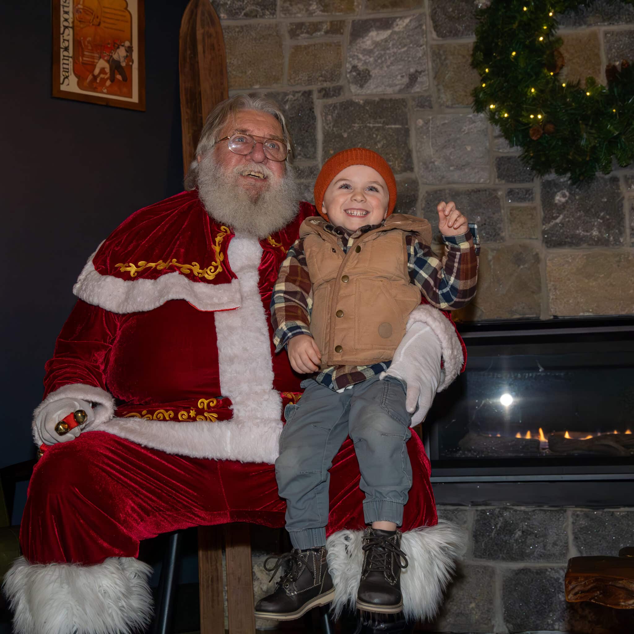 Photo features a young boy sitting on Santas lap in front of the fireplace.