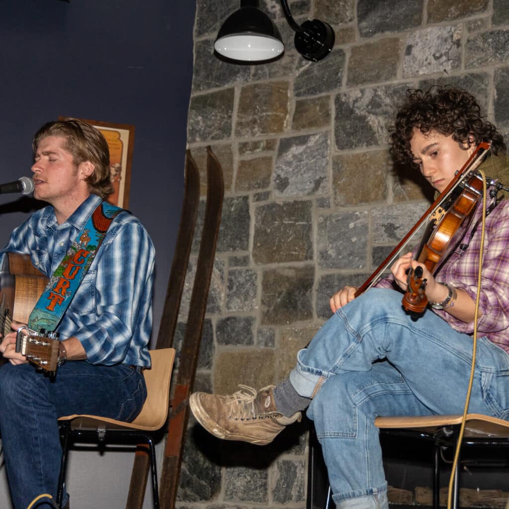 Two people playing live music, with a guitar and a fiddle.